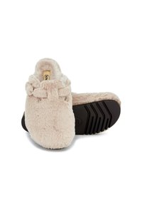 Chaussons beiges moelleux avec une forme arrondie, en matériau en fausse fourrure léger, avec une volure décorative autour de la cheville et une semelle en caoutchouc noir texturé.
