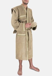 Beige Frottee-Bademantel mit einem Gürtel, Kapuze und zwei Taschen. Besitzt dekorative Streifen in Gold und Grün entlang der Ärmel und vorne.