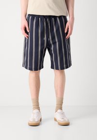 Shorts rayés bleu marine en tissu tissé, avec une taille élastique à cordon et des poches latérales, associés à des baskets blanches et des chaussettes beiges.