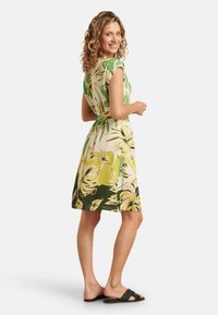 Short-sleeved dress featuring a tropical leaf pattern in greens and yellows, cinched at the waist with a tie, ending above the knee.
