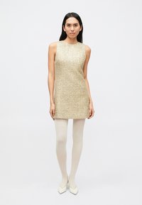 Ärmelloses Kleid mit goldener Textur und gerader Silhouette, kombiniert mit hellen Strumpfhosen und spitzen weißen Schuhen. Einfaches Design, minimalistische Details.