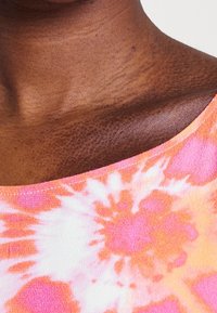 Haut coloré en tie-dye avec un mélange de nuances roses et orange, fabriqué dans un tissu léger et doux, avec des détails subtils au niveau de l'encolure.