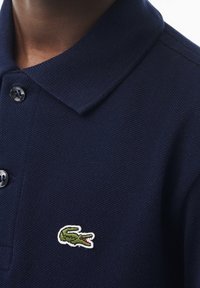 Námořnická polokošile z texturované bavlny, s klasickým límečkem, dvěma černými knoflíky a zeleným krokodýlem na levé části hrudi.