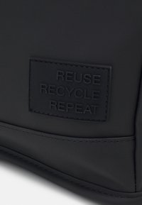 Sort silikonepose med et præget mærkat med teksten "GENBRUG GENANVEND GENOPTAG." Glat tekstur med rene linjer, minimalistisk design.