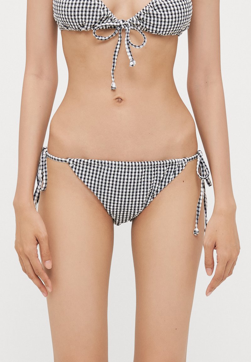 Top de bikini en vichy noir et blanc avec fermeture à nouer réglable, bas de bikini taille basse assorti avec liens sur les côtés, présentant un tissu texturé.