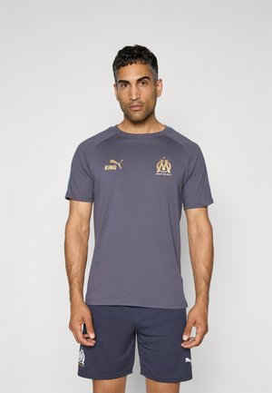 T-shirt gris avec des accents bleus et des logos dorés, doté d'un col rond et de manches courtes, associé à un short marine avec un logo au bas.