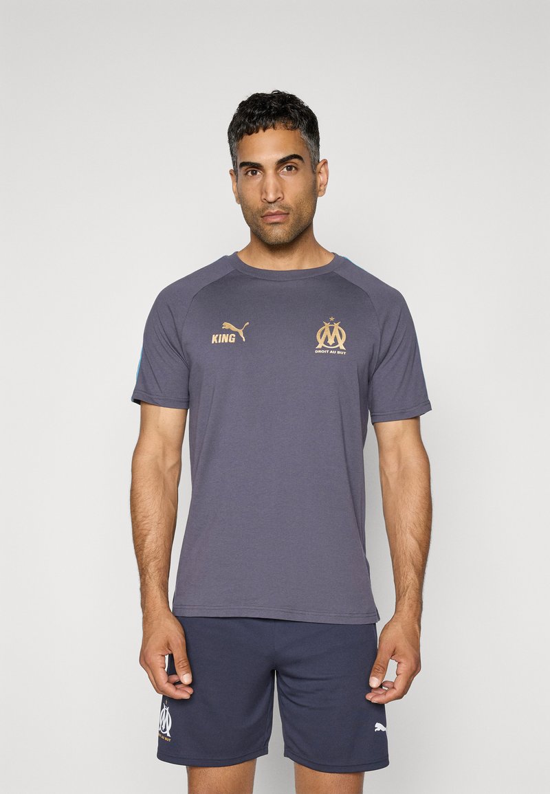 Grå T-shirt med blå accenter og gyldne logoer, der har rund hals og korte ærmer, parret med navy shorts med logo ved kanten.