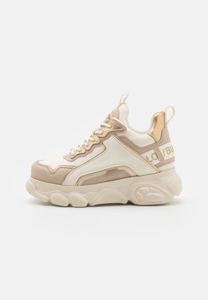 Chunky beige en witte sneaker met gestructureerde overlays, vetersluiting aan de voorkant, gevoerde kraag en logo-accenten aan de zijkant en hiel.