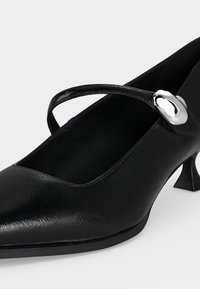 Chaussure Mary Jane en cuir verni noir avec un talon moyen large et une boucle argentée arrondie sur la bride.