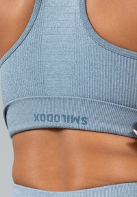 Lichtblauwe geribbelde sportbeha met een brede band. Bevat een subtiel logo in donkerder blauw. Gladde textuur en een racerback ontwerp.