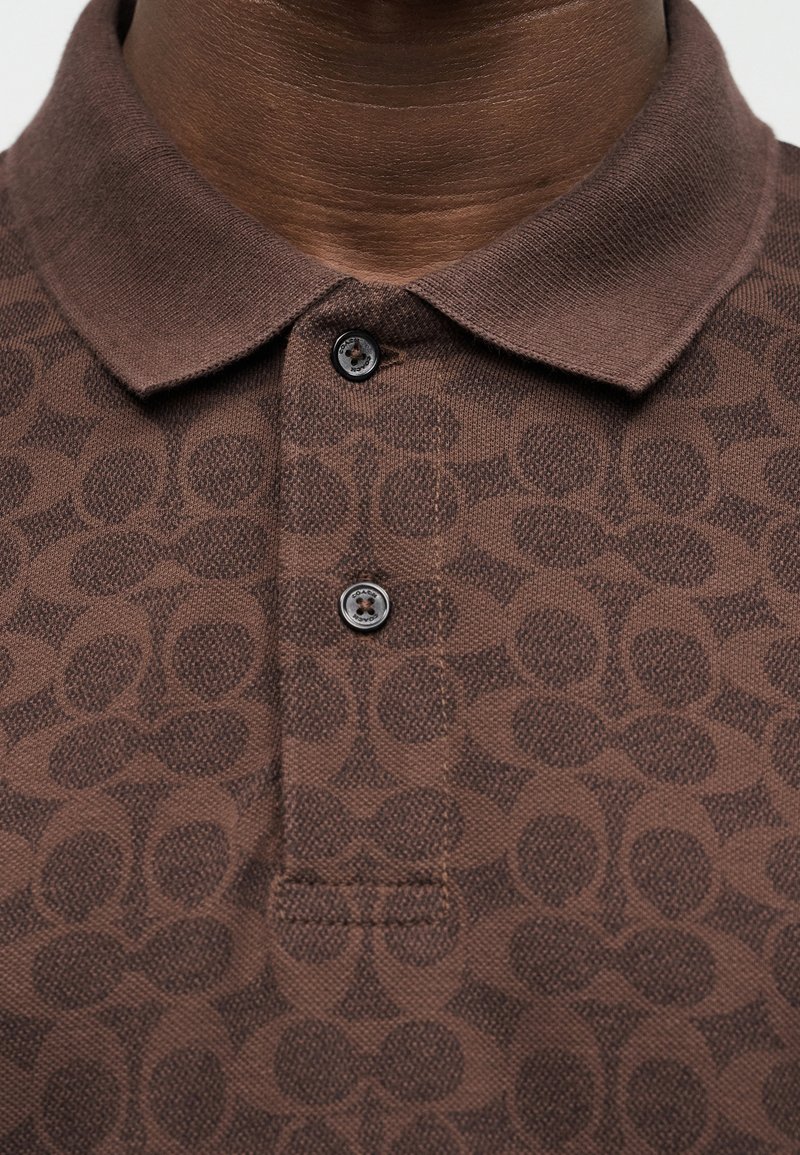 Close-up of a brown polo shirt with a subtle geometric pattern and two black buttons fastened at the collar.