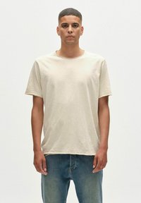 Beidzīgas īsa piedurkne T-krekls no mīkstā, vieglā auduma ar apaļu kakla izgriezumu un brīvu piegriezumu, kombinēts ar zilo džinsu biksēm.