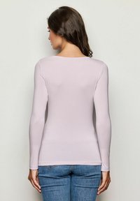 Hellpurpurnes Langarmshirt mit rundem Halsausschnitt, figurbetontem Design und glatter Textur, kombiniert mit blauen Jeans.