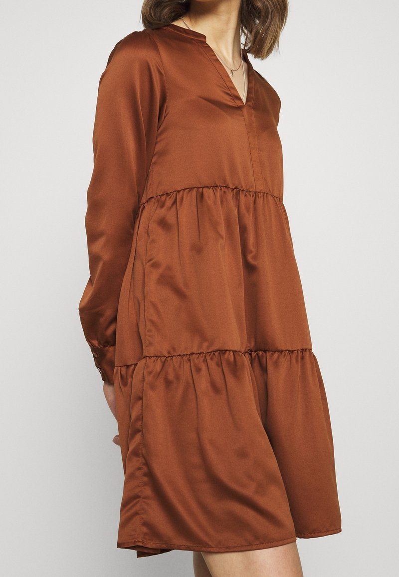 Brun satin klänning med v-ringning, långa ärmar och flerlagers volangdesign. Slät textur och lös passform, som slutar ovanför knäet.