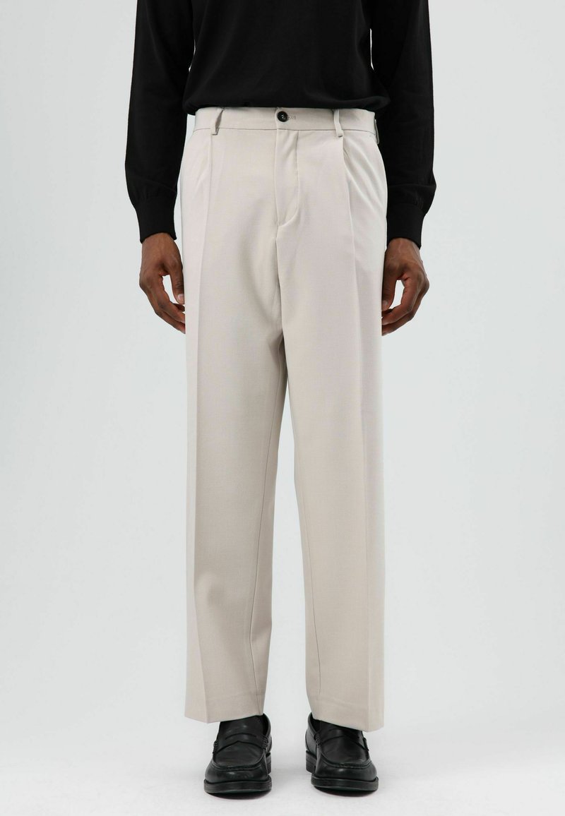 Lichtbeige geplooide broek met een ontspannen pasvorm, gemaakt van geweven stof. Voorzien van zijzakken, een knoopsluiting aan de voorkant en een gladde afwerking.