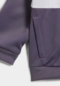 Giacca viola con tessuto testurizzato, polsini a costine, un pannello bianco nella parte superiore e una tasca laterale con apertura verticale.