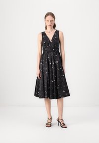 Black dress featuring a V-neckline, sleeveless design, and star pattern in white. Flared skirting extends to mid-calf, accompanied by black strappy heels.