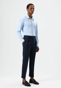 Lichtblauw overhemd met lange mouwen, marineblauwe gevouwen broek met een riemlusdetail en zwarte loafers. Glad stof, op maat gesneden pasvorm, omgeslagen broekspijpen.