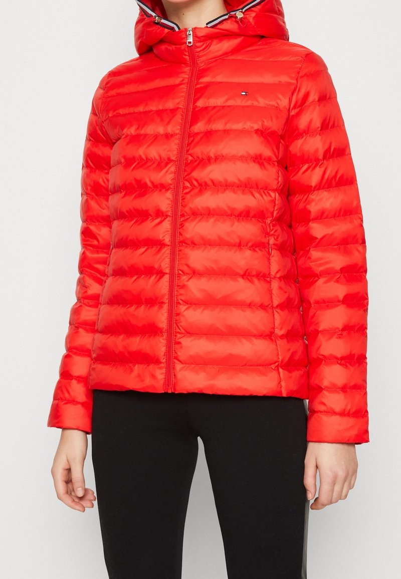Chaqueta de plumas roja con cremallera frontal y capucha, que presenta un diseño acolchado, textura brillante y acentos de cremallera en blanco y negro contrastantes.