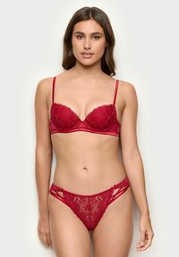 Conjunto de lencería de encaje rojo que incluye un sujetador con aros y tirantes ajustables, acompañado de un tanga decorativo a juego.