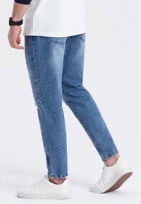 Vaqueros de mezclilla azul claro con corte ceñido, que presentan detalles desgastados y un sutil desvanecimiento. Combinados con zapatillas blancas.