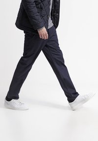 Spodnie w kolorze granatowym o prostym kroju, wykonane z lekkiego, gładkiego materiału, zestawione z białymi tenisówkami na jednolitym tle.