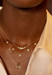 Collares de oro laminado con diferentes longitudes de cadena, que presentan pequeños acentos florales brillantes y un colgante con detalles colgantes.