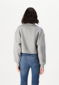 Felpa grigia a maniche lunghe, corta, con colletto a coste e spalle scese, abbinata a jeans blu slim che mostrano tasche posteriori e una silhouette aderente.