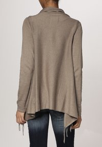 Cardigan lungo color marrone chiaro, con maniche lunghe e retro drappeggiato, tessuto a maglia strutturata e lacci laterali per la regolazione. Vestibilità casual con orlo arrotondato.