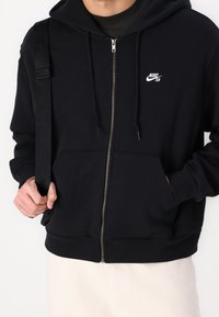 Felpa nera con zip realizzata in morbido tessuto, con zip frontale, due tasche laterali e un piccolo logo Nike SB bianco sul petto.
