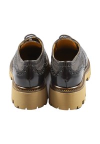 Stivali alla caviglia in pelle nera con dettagli brogue, suole spesse color nocciola e punta arrotondata. Presentano un piccolo tacco e linguette laterali per il sollevamento.