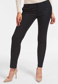 Black polka dot trousers feature a fitted design and soft texture, complemented by a smooth waistband. Paired with beige high heels.