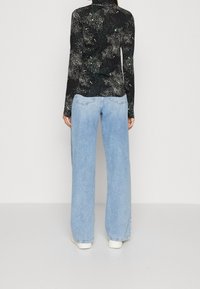 Svart långärmad topp med galaxtryck, tillsammans med ljusblå vida jeans. Jeans med bakfickor och en avslappnad passform.