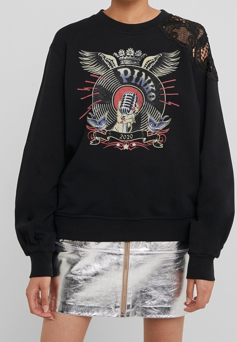 Felpa nera con design grafico colorato che presenta un microfono, ali e uccelli. Dettaglio in pizzo sulla spalla sinistra. Gonna riflettente argento sottostante.