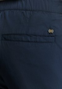 Navy blauwe stoffen shorts met een achterzak en een rechthoekige zwarte hardware-accent. Glad textuur, lichtgewicht ontwerp en op maat gemaakte pasvorm.
