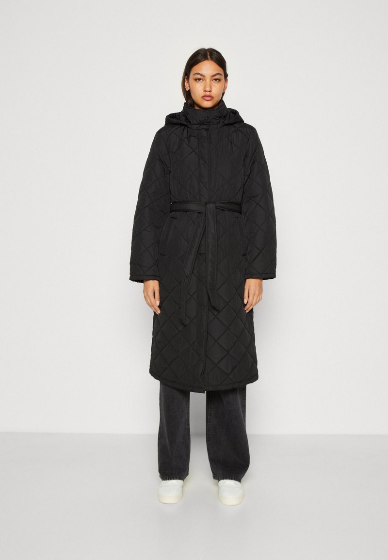 Cappotto lungo trapuntato nero con cappuccio, vita regolabile con cintura e tasche laterali, caratterizzato da un motivo a rombi e una vestibilità comoda. Abbinato a pantaloni scuri.
