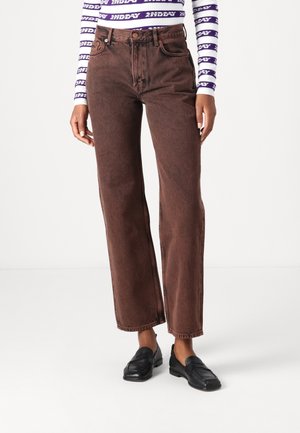 Personne portant un jean marron taille haute à jambes larges, des mocassins noirs et un haut rayé violet et blanc à manches longues avec motif texte.
