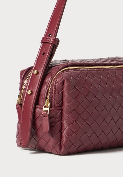 Geantă de mână din piele burgundă țesută, cu fermoare aurii, curea ajustabilă și formă rectangulară. Prezintă o textură subtilă și cusături detaliate.