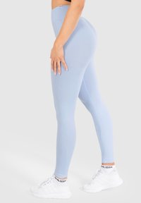 Světle modré legíny s hladkou, elastickou tkaninou a vysokým pasem, v kombinaci s bílými sportovními botami a ponožkami s logem.