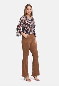 Przezroczysta, wzorzysta bluzka z falbaniastym dekoltem i dzwonowymi rękawami; zestawiona z brązowymi spodniami w stylu zamszowym o fasonie dzwonów oraz cielistymi, wiązanymi szpilkami.