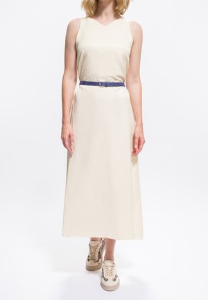 Donna che indossa un abito midi senza maniche crema con una cintura blu e sneakers beige con stampa leopardata, che cammina in avanti su sfondo bianco.