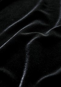 Tissu en velours noir avec des plis doux et une texture lisse et brillante reflétant la lumière le long des plis.