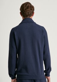 Marineblauer Pullover aus weichem Stoff, mit hohem Kragen, langen Ärmeln sowie gerippten Bündchen und Saum, und einer glatten, strukturierten Oberfläche.