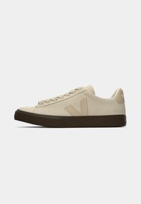 Sneaker in suede beige con punta tondeggiante, allacciatura frontale e suola in gomma marrone scuro. Logo V evidente sul lato e branding sul tallone.