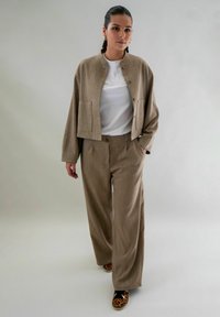 Beige textuur cropped jacket met zijzakken, gecombineerd met bijpassende wijde broek. Witte t-shirt eronder, schoenen met dierenprint.