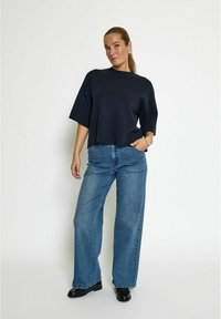 Tmavě námořnický oversized top s krátkým rukávem, kombinovaný se světle modrými širokými džíny s kapsami a vysokým pasem. Černá obuv.