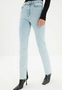 Jeans de tiro alto de color azul claro con corte recto, que presentan aberturas laterales en el dobladillo, combinados con botas de tobillo negras de punta afilada.