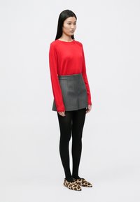 Jersey rojo de manga larga, minifalda gris, medias negras y zapatos planos con estampado de leopardo; presenta un diseño entallado y texturas suaves.