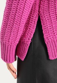 Fuchsia stickad tröja med ribbade muddar och fåll, har en delad design bak, visad bredvid en svart läderkjol.