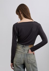 Black long-sleeve top with a wide neckline and gathered detail at the shoulders, paired with light blue high-waisted jeans.